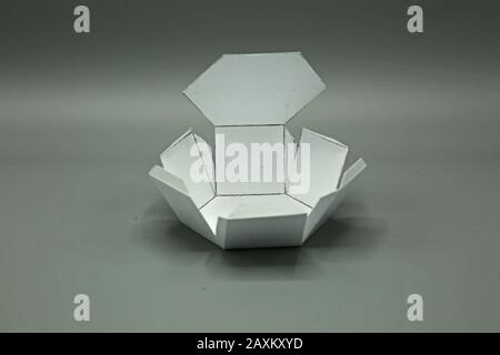 Forma geometrica ritagliata di carta e fotografata su sfondo grigio.prisma Esagonale. Forma bidimensionale pieghevole per formare una forma 3D o un solido. Unfo Foto Stock