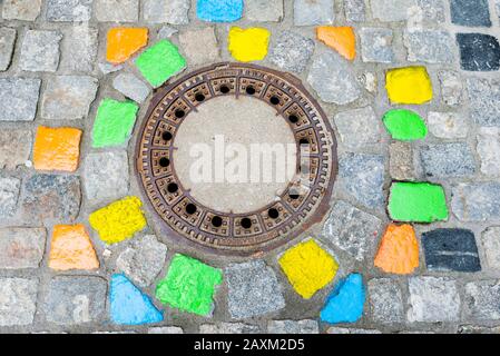 Pietre da pavimentazione dipinte in modo luminoso intorno a una copertura di burrone nella Città Vecchia di Passau Foto Stock