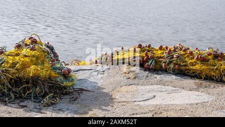 Reti da pesca messe su terra di cemento per ottenere asciutto. Reti a rete in nylon giallo con corde e tappi sotto le travi solari e accanto a un mare azzurro calmo. Foto Stock