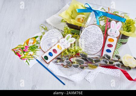 Vista dall'alto del set di pittura regalo per colorare le uova di pasqua, isolato su tavola di legno. Vernici acquerello vicino a tovagliolo, scatola con fiori, ramo salice e pennello. Concetto di vacanze di primavera e pasqua. Foto Stock