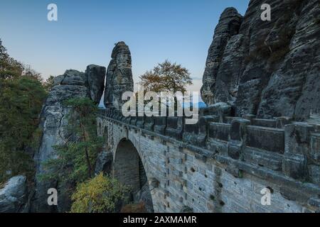 Vista laterale del Ponte di Bastei UNESCO nel Parco Nazionale della Svizzera Sassone. Sentiero in serata con formazione rocciosa. Cielo blu con alberi e foreste Foto Stock