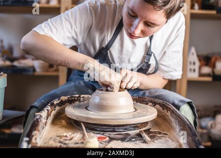 Potter che lavora su una ruota di Potter che fa un vaso. Giovane donna che forma l'argilla con le mani creando brocca in un laboratorio. Foto Stock