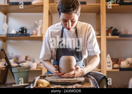 Donna vasaio che lavora su una ruota di Potter che fa un vaso. Master tira la brocca fuori dal cerchio bagnandola con acqua e tenendola delicatamente nelle mani Foto Stock