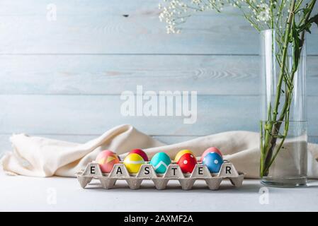 Uova di Pasqua colorate e luminose in un vassoio su uno sfondo di legno. Biglietto di primavera festivo con testo Foto Stock