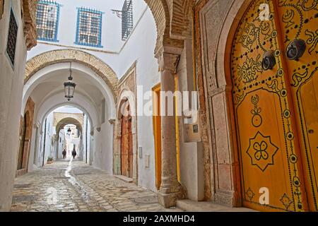 Tipica strada acciottolata e stretta con porte colorate, colonne e portici all'interno della storica medina di Tunisi, Tunisia Foto Stock