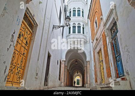 Tipico vicolo acciottolato e stretto (visto da via Pacha) con porte colorate, colonne e portici all'interno della storica medina di Tunisi, Tunisia Foto Stock