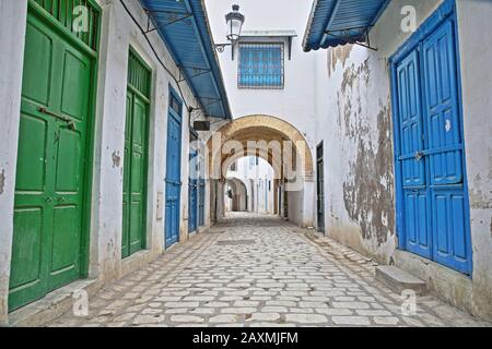 Tipica strada acciottolata e stretta (via Pacha) con porte colorate, colonne e portici all'interno della storica medina di Tunisi, Tunisia Foto Stock