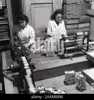 1950s, storico, due lavoratori di sesso femminile che indossano camici bianchi utilizzando macchinari di piccole dimensioni per confezionare e avvolgere medicinali, pacchetti di compresse, 'Cubebs Compound compresse', prodotto da Arthur Cox di Brighton, un produttore leader e fornitore di medicinali in questa era, Inghilterra, Regno Unito. Foto Stock