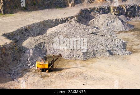 macchina escavatore giallo macerie di scalpellatura vicino alle rocce in una cava per l'estrazione del granito Foto Stock