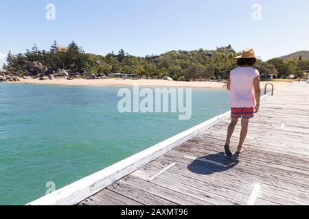 Capelli ricci uomo, con cappello, camminare su banchina di legno di magnetico è. Foto Stock