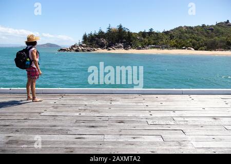 Giovane zaino in spalla, con cappello di paglia e costume da bagno, su banchina di legno Foto Stock