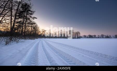 Trattore piste nella neve, crepuscolo sul campo nevoso, paesaggio invernale. Foto Stock