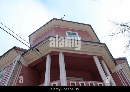 Casa a due piani in legno di colore rosa scuro con balcone e colonne contro un cielo blu nuvoloso. Vista dal basso. Stock foto per il web e stampa con spazio vuoto per il testo. Foto Stock