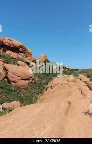 Il Trading Post Trail accanto a grandi formazioni rocciose di arenaria rossa con arbusti che crescono nelle fessure nel Red Rocks state Park, Morrison, Colorado Foto Stock