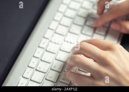 La ragazza lavora a casa al computer. Le mani femminili stanno digitando sulla tastiera, primo piano. Foto Stock