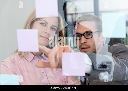 Giovane donna d'affari e giovane uomo d'affari leggono post-it in un vetro, ritratto Foto Stock