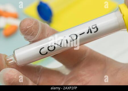 Nome ufficiale COVID-19 / Coronavirus. Fiala con virus in mano nel guanto da laboratorio Foto Stock