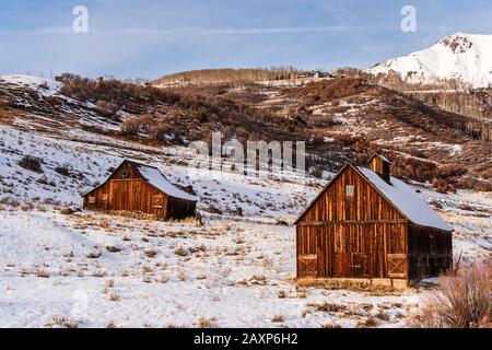 Un paio di rustici granai di legno catturano la luce del sole serale ai piedi delle montagne di San Juan a Telluride, Colorado, Stati Uniti. Foto Stock