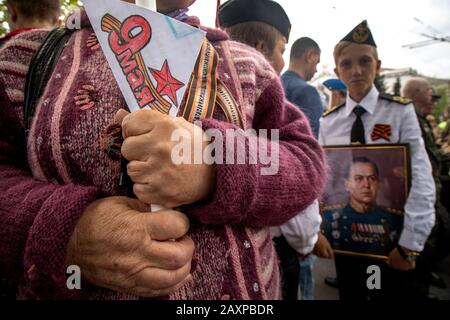 Sevastopol, Crimea, 9 maggio 2019 la donna anziana tiene un ritratto con la fotografia dei suoi parenti, di quelli uccisi nella seconda guerra mondiale, e una cartolina con iscrizione in russo 'il 9 maggio' durante l'azione il reggimento immortale nella città di Sevastopol. Un ragazzo sullo sfondo ha un ritratto di Maresciallo dell'Unione Sovietica Georgy Zhukov Foto Stock