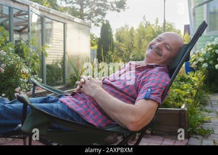 Uomo adulto in abbigliamento casual seduto su una sedia a sdraio e riposante con un pisolino il giorno d'estate. Foto Stock