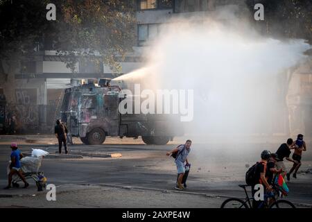 Camion corazzato di polizia con cannoni ad acqua che spruzzano acqua sui manifestanti durante le recenti dimostrazioni a Plaza de Italia a Santiago del Cile. Foto Stock