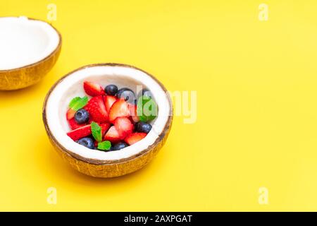 Ciotola di cocco con frutti di bosco freschi su sfondo giallo con spazio copia Foto Stock