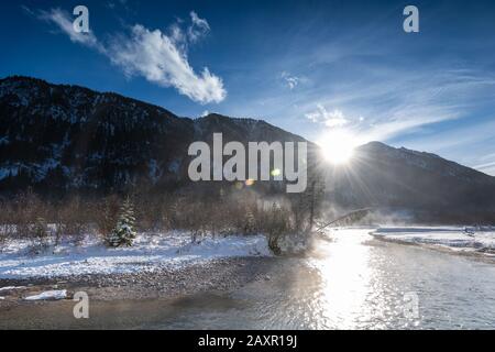 Sole e Sunstar sull'Isar All'Autunno nel Karwendel nel mezzo dell'inverno, il fiume innevato riflette la luce del sole e alcuni alberi di abete si trovano sul Foto Stock