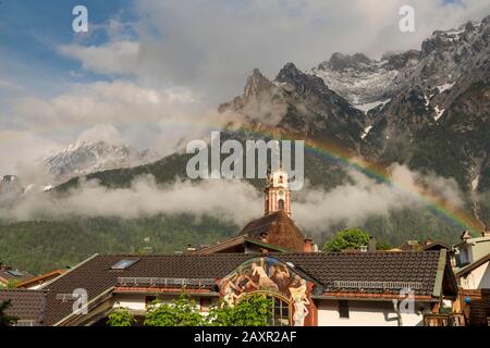 Arcobaleno sopra la torre della chiesa di Mittenwald nel Karwendel bavarese. Sullo sfondo le montagne del Karwendel, parzialmente innevate. Foto Stock