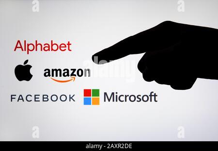 Logo aziendali Big Tech: Alfabeto, Amazon, Apple, Facebook e Microsoft su uno schermo sfocato e una silhouette della mano. Antitrust e regolamentazione. Foto Stock