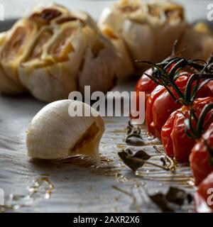 Bulbi d'aglio arrosto e pomodori ciliegini. Foto Stock