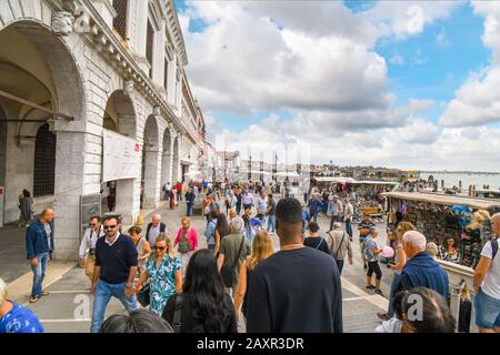 Una grande folla di turisti acquista bancarelle di souvenir e visita il lungomare Riva degli Schiavoni a Venezia. Foto Stock