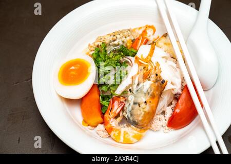Pesce noodle tailandese mescolato tra gamberi bolliti, calamari, maiale, uova e verdure colorate in ciotola bianca.