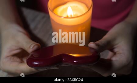 Cuore rosso nelle mani di una ragazza con una candela bruciante. Un cassiere di fortuna tiene un cuore nelle sue mani e supposizioni all'amore futuro con una candela illuminata. Foto Stock