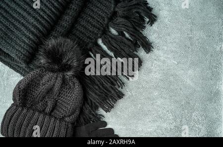 Accessori donna calda a posa piatta inverno o autunno - sciarpa nera a maglia, cappello su sfondo grigio brillante in pietra, spazio copia. Foto Stock