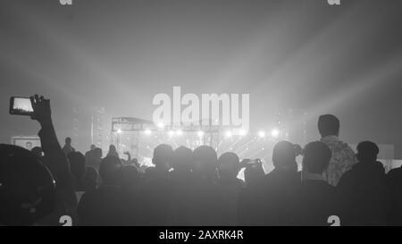 Silhouette di grande pubblico folla di persone felici in piedi al concerto motivi di rallegramento clapping utilizzare smartphone alzando le mani in aria di fronte musica b Foto Stock