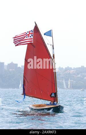 una vecchia barca a vela in legno con vela rossa e Union jack si insigne facendo una buona velocità in una forte brezza che naviga nel porto di Sydney, Gaffers Day 2011 Foto Stock