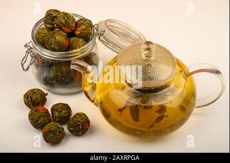 Tè floreale preparato in una teiera di vetro, palle da tè e un vaso di tè su uno sfondo bianco. Primo piano Foto Stock