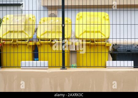 Giallo Garbage lattine stand in fila dietro un recinto di maglia. Foto Stock