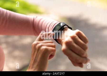 Primo piano di mani di una donna caucasica matura di mezza età che lavora in un parco, controllando il suo smartwatch, preparandosi ad allenarsi Foto Stock