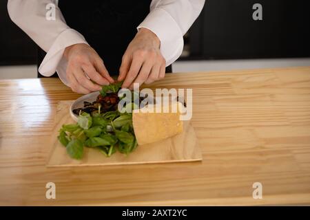 Vista frontale parte centrale di uno chef femmina caucasico in una lezione di cucina in una cucina ristorante, preparando un'insalata guarnita con foglie di insalata fresca. Ca Foto Stock