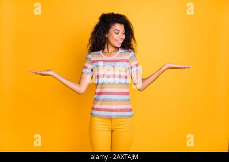 Ritratto di lei bella bella allegra allegra ragazza con capelli ondulati in camicia a righe tenendo su palme due oggetti invisibili che pesano isolato su Foto Stock