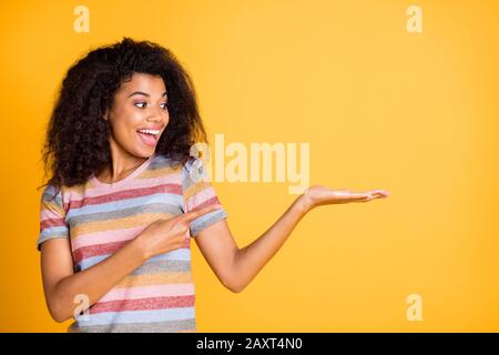 Ritratto di lei bella allegra allegra allegra stupita ragazza con capelli ondulati indossando camicia a righe tenendo sul palmo invisibile soluzione isolata su Foto Stock