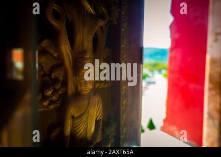 Wat Chalong, Phuket/Thailandia-15December2019: Scatto di dettaglio di una scultura in legno e inlay oro di buddha signore in una cornice finestra della grande pagoda. Foto Stock