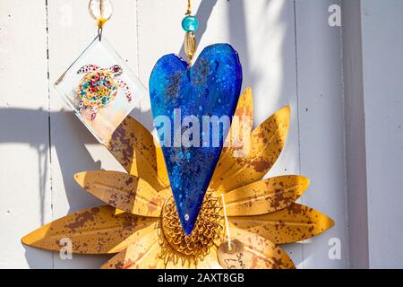 Decorazione A Cuore In Vetro A Motivi Blu Visualizzata Su Una Porta In Legno Bianco Con Grande Fiore Di Metallo E Tartaruga Pendente In Vetro In Un Negozio Di Articoli Da Regalo Boutique Foto Stock