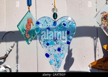 Blue Speckled Glass Heart Decoration On White Wooden Door, Large Metal Sunflower & Glass Seahorse Pendant With Shadows At A Boutique Gift Shop. Foto Stock