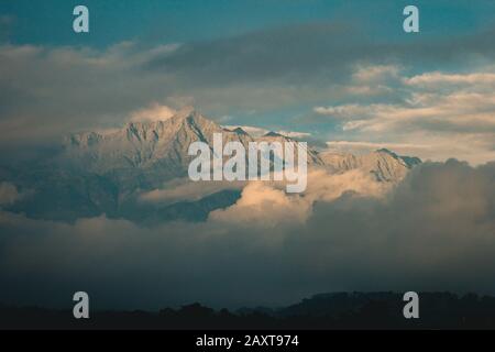 Montagna coperta di nuvole che sono illuminate dal sole del tramonto. Foto Stock