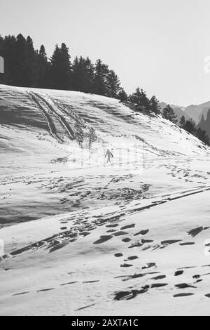 Una foto in bianco e nero di un uomo che cammina in salita attraverso un tratto di neve. Foto Stock