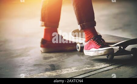 I piedi di un adolescente alla moda in jeans, calze rosse, e sneakers sportive rosa, e accanto a un pattino grigio, illuminato dalla luce del sole. Foto Stock