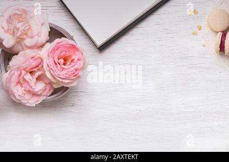 Rosa rose, blocco note, orologio e macaron su tavola di legno bianco Foto Stock