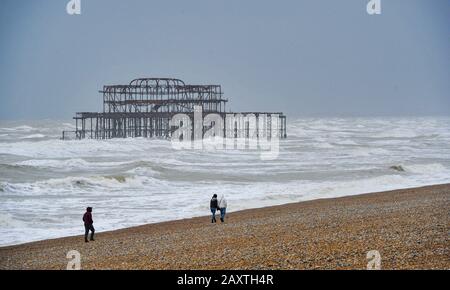 Brighton UK 13th Febbraio 2020 - Walkers affronta il clima umido e ventoso sulla spiaggia di Brighton vicino al West Pier mentre Storm Dennis si avvicina alla Gran Bretagna con venti forti e inondazioni che dovrebbero causare ulteriori danni questo prossimo fine settimana: Credit Simon Dack / Alamy Live News Foto Stock